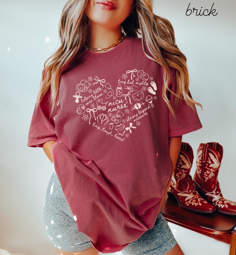 May include: Brick-colored t-shirt featuring a heart-shaped design with the words "nicu nurse" and other text and illustrations. The shirt has short sleeves and a relaxed fit. The word "brick" is written in the upper right corner.