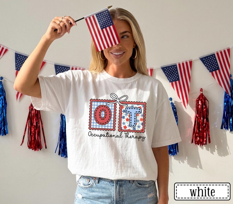 May include: White t-shirt with a graphic design featuring the letters "OT" in red and blue postage stamp style boxes. The shirt also has the words "Occupational Therapy" printed below the letters. The person is holding a small American flag.
