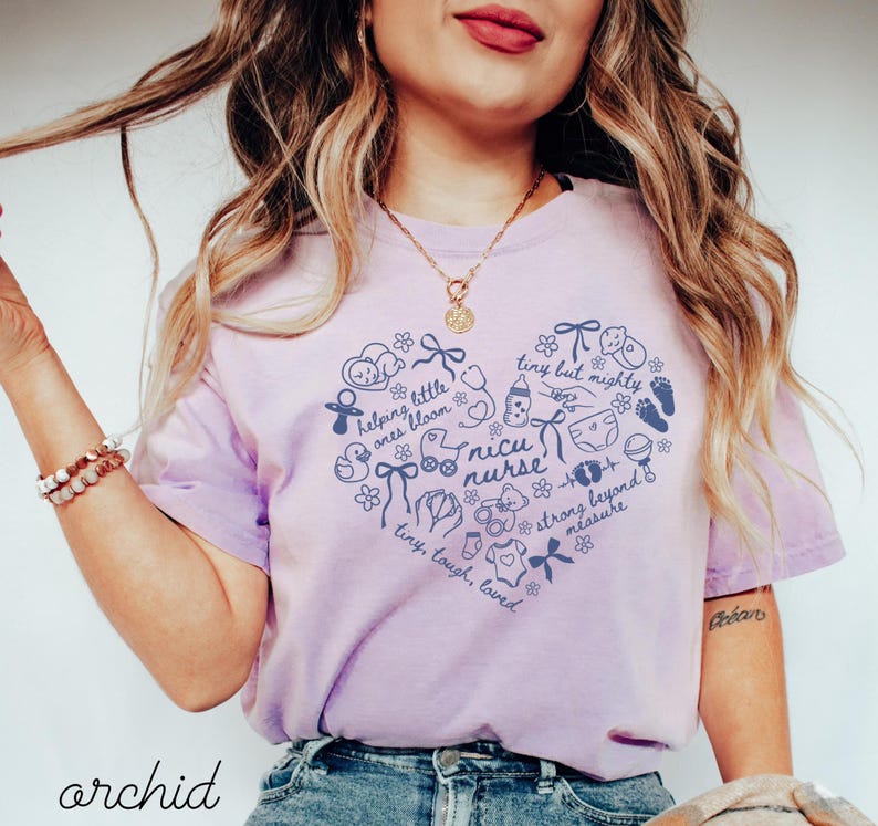 May include: A light purple t-shirt with a heart-shaped design filled with baby-related illustrations and the words "NICU nurse." The shirt also includes the words "helping little ones bloom" and "tiny but mighty."