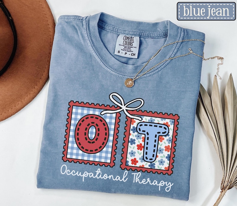 May include: A blue jean Comfort Colors t-shirt with the words "OT" in red and blue postage stamp designs. The "O" is red with a white gingham background, and the "T" is blue with a floral background. The words "Occupational Therapy" are printed below.