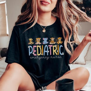 May include: Black t-shirt with a graphic of cartoon animals and the text "PEDIATRIC emergency nurse".