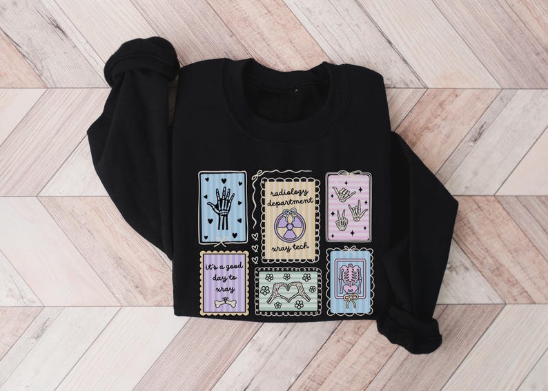 May include: Black sweatshirt featuring colorful illustrations related to radiology. Designs include a hand, a radiation symbol, hand gestures, a skeleton, and the text "It's a good day to xray" and "radiology department xray tech".