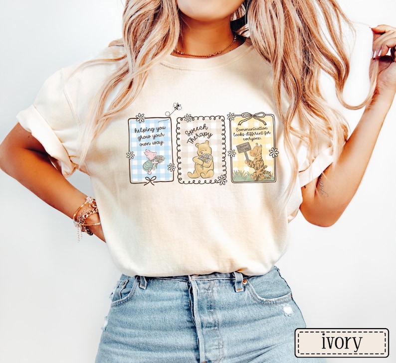 May include: Ivory-colored t-shirt featuring three framed illustrations with text. The first frame reads "helping you grow your own way" with a pig and flowers. The second says "Speech Therapy" with a bear. The third says "Communication looks different for everyone" with a tiger.