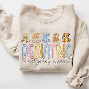 May include: A beige sweatshirt with a graphic of cartoon animals and the text "PEDIATRIC emergency nurse".