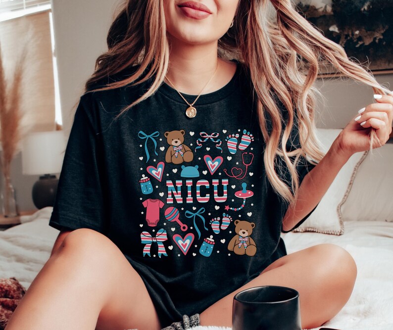 May include: Black t-shirt with a colorful design featuring a teddy bear, a baby bottle, a rattle, and the word "NICU".