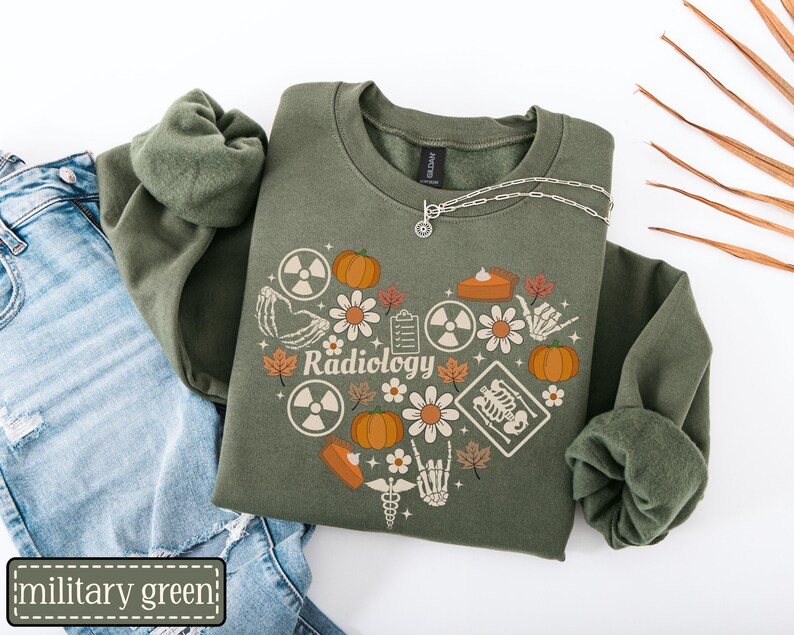 May include: A military green crewneck sweatshirt featuring a heart-shaped graphic composed of pumpkins, flowers, radiation symbols, skeleton hands, a clipboard, a slice of pie, and an X-ray, with the word Radiology printed in the center.