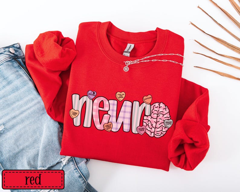 May include: A red sweatshirt with the word "neuron" in a playful font, featuring a brain graphic and heart-shaped candies. A silver chain necklace is draped across the top. The word "red" is in a red rectangle at the bottom.