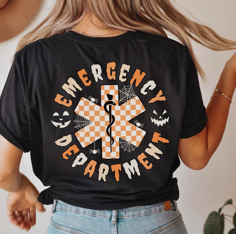 May include: Black t-shirt with an orange and white checkered star of life design, the words "EMERGENCY DEPARTMENT" in a circular pattern, and Halloween-themed accents like jack-o'-lanterns and spiderwebs.