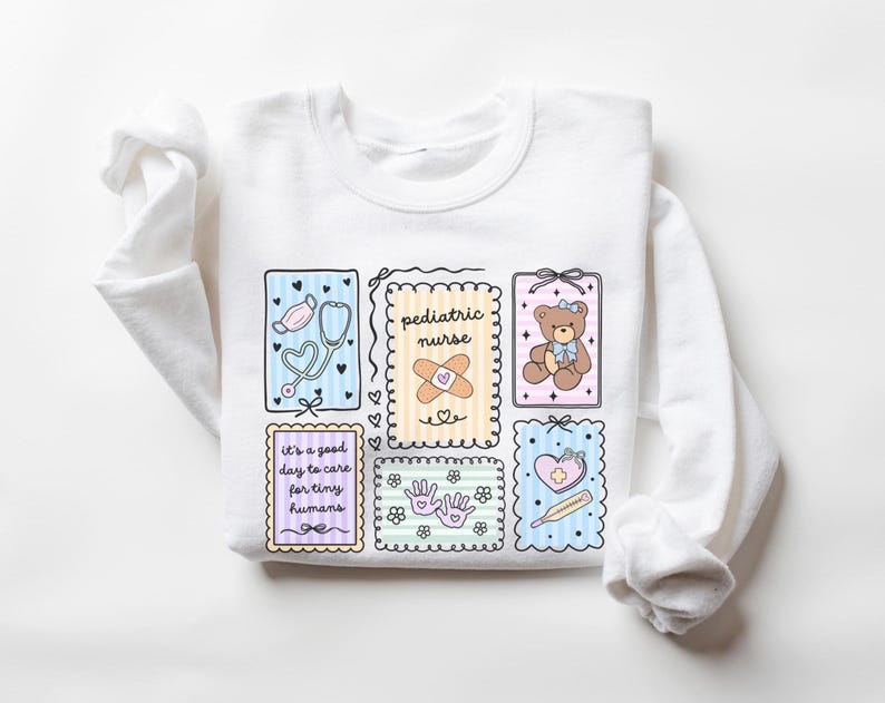 May include: White long-sleeved sweatshirt featuring colorful illustrations related to pediatric care. The design includes a stethoscope, teddy bear, bandage, and the text "pediatric nurse" and "it's a good day to care for tiny humans."