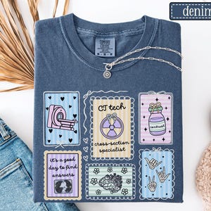 May include: Denim blue t-shirt with a graphic design featuring medical imaging symbols and the text "CT tech cross section specialist". The shirt also has the text "it's a good day to find answers".