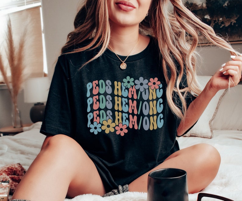May include: Black t-shirt with a retro design featuring the text "PEDS HEM/ONG" repeated three times with colorful flowers in between each line.