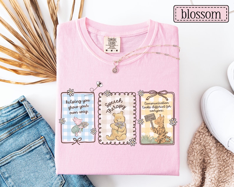 May include: Pink Comfort Colors t-shirt featuring three framed illustrations with Winnie the Pooh characters and text. The text includes "helping you grow your own way," "Speech Therapy," and "Communication looks different for everyone."