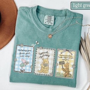May include: Light green t-shirt with three framed graphics featuring Winnie the Pooh characters. The graphics include text that reads "helping you grow your own way," "Speech Therapy," and "Communication looks different for everyone."