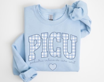 May include: A light blue sweatshirt with the word "PICU" in large, block letters filled with a blue and white gingham pattern. Below the letters, the text reads "pediatric intensive care unit" with a gingham heart.