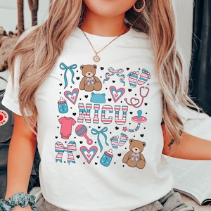 May include: White t-shirt with a pink, blue, and white graphic design featuring a teddy bear, baby bottle, rattle, and the word "NICU".