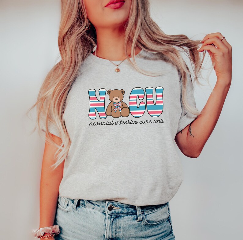 Puede incluir: Una camiseta gris con un gr&aacute;fico de un osito de peluche con un lazo rosa y el texto "NICU" en rayas azules, rosas y blancas. El texto "unidad de cuidados intensivos neonatales" est&aacute; escrito debajo del gr&aacute;fico.