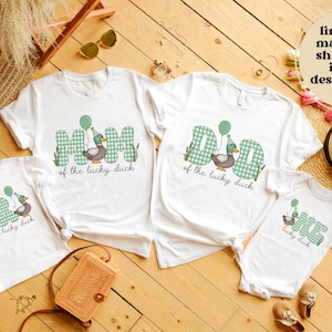 May include: White t-shirts with green and white checkered text that says "Mom of the lucky duck", "Dad of the lucky duck", and "One of the lucky duck". Each shirt features a cartoon duck wearing a party hat and holding a balloon.