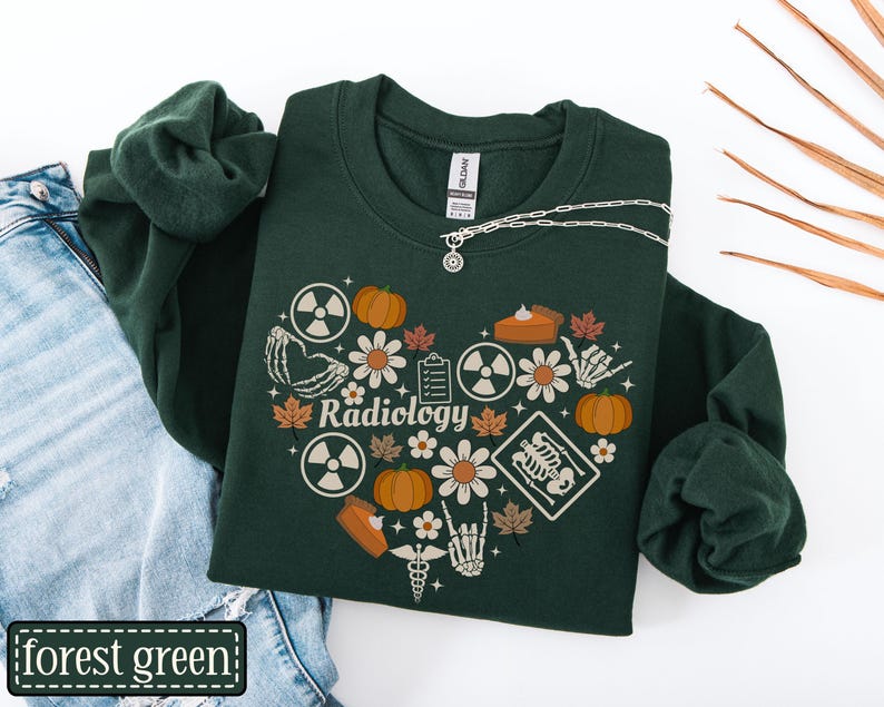 May include: A forest green crewneck sweatshirt featuring a heart-shaped graphic composed of pumpkins, autumn leaves, daisies, skeleton hands, radiation symbols, a clipboard, and a medical caduceus with the word Radiology printed in the center.