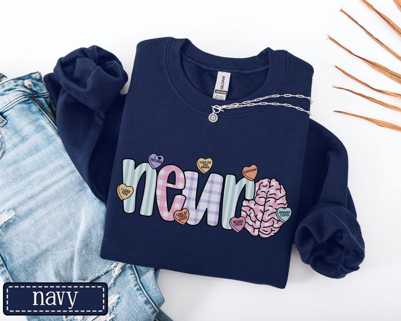 May include: Navy blue sweatshirt with the word "neur" in a colorful, playful font, and a brain graphic. The word "neur" is decorated with heart-shaped candies. A silver necklace is draped across the sweatshirt.