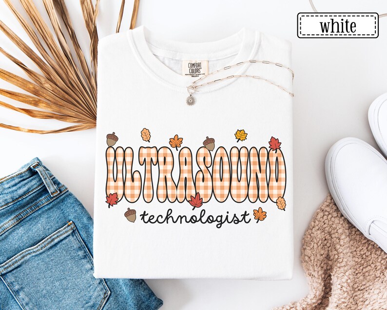 Puede incluir: Sudadera blanca de cuello redondo con las palabras "ULTRASOUND technologist" en una fuente naranja a cuadros, decorada con hojas de oto&ntilde;o y bellotas. La sudadera es de la marca Comfort Colors. La palabra "white" est&aacute; en un cuadro en la esquina superior derecha.