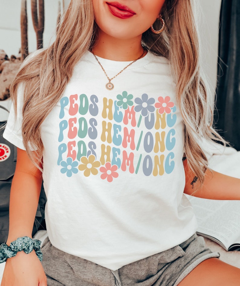 May include: A white t-shirt with the text "PEDS HEM/ONG" repeated three times in a retro font. The text is in different colors, including pink, blue, yellow, and green. Each line of text is decorated with a colorful flower.