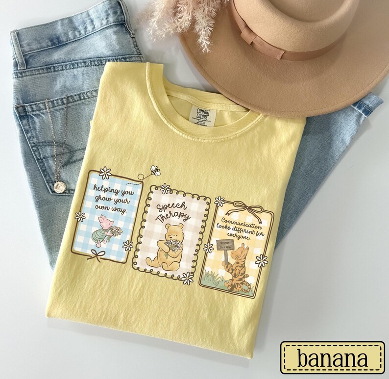 May include: A yellow Comfort Colors t-shirt featuring three framed illustrations with Winnie the Pooh characters and the phrases "Helping you grow your own way," "Speech Therapy," and "Communication looks different for everyone." The shirt is paired with light wash jeans and a tan hat.