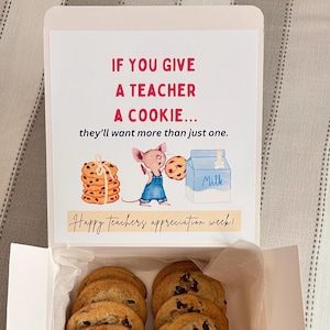 May include: A white gift box with a colorful illustration of a mouse holding a cookie and a carton of milk. The box has a message that reads "If you give a teacher a cookie... they'll want more than just one." and "Happy teachers appreciation week!" The box is open and filled with chocolate chip cookies.