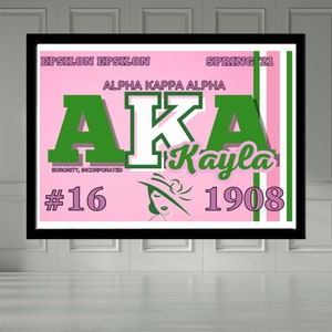 May include: A framed pink and green Alpha Kappa Alpha sorority print. The print features the letters AKA in green, the name "Kayla", and the year 1908. The words "Epsilon Epsilon" and "Spring '21" are also visible.
