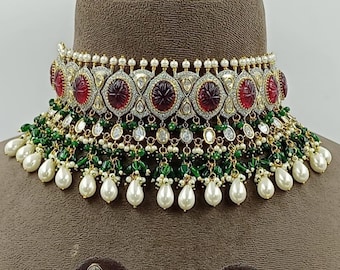 Könnte beinhalten: Ein traditionelles indisches Braut-Halsketten- und Ohrring-Set. Die Halskette besteht aus einem goldenen und silbernen Choker mit roten und grünen Steinen sowie einer Fransen aus Perlen und grünen Perlen. Die Ohrringe sind ähnlich gestaltet mit roten und grünen Steinen, Perlen und grünen Perlen.