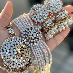 May include: A gold and white necklace and earrings set with a round, mirrored design. The necklace has multiple strands of white pearls and a large pendant with a mirrored center. The earrings have a similar mirrored design with a smaller pendant.