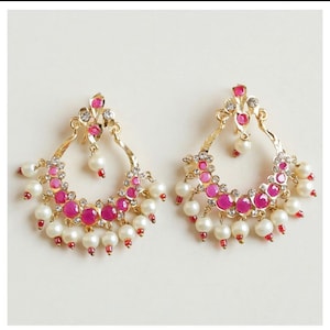 May include: A pair of gold earrings with pink and white stones. The earrings are in the shape of a crescent moon and have a dangling pearl drop.
