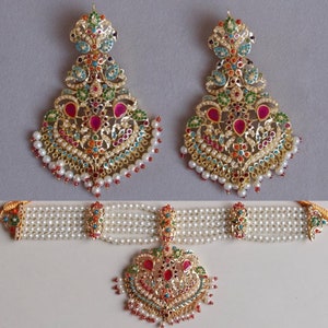 May include: A set of gold earrings and a necklace with a pendant. The earrings and pendant are decorated with intricate designs and colourful gemstones. The necklace is made of pearls.