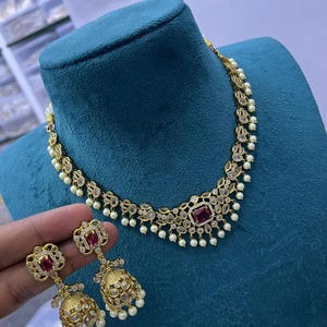 May include: A gold necklace with a pink stone and white pearls. Matching earrings with a pink stone and white pearls.