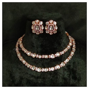 May include: A rose gold necklace and earrings set with a double row of clear stones. The stones are set in a rose gold metal frame.