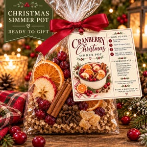 May include: A clear plastic bag filled with dried cranberries, orange slices, apple slices, cinnamon sticks, and ginger, tied with a red ribbon. A tag attached reads Cranberry Christmas Simmer Pot with instructions and ingredients listed.