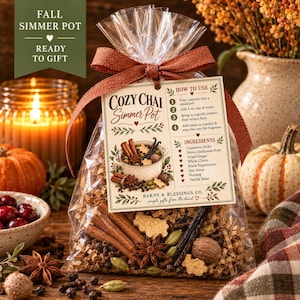 May include: A clear plastic bag filled with dried spices including cinnamon sticks, star anise, cardamom pods, and cloves, tied with a copper ribbon. A tag attached to the bag features the text Cozy Chai Simmer Pot, instructions, and ingredients.