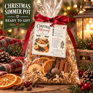 May include: A clear plastic bag filled with dried orange slices, apple slices, cinnamon sticks, and spices for a Christmas simmer pot. A tag attached with a red ribbon displays the text Christmas Morning Simmer Pot, ingredients, and instructions.
