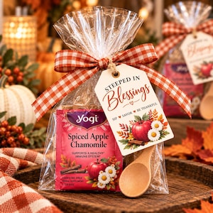 May include: A clear plastic bag containing a Yogi Spiced Apple Chamomile tea bag, tied with a red and white gingham ribbon. A white tag reads "STEEPED IN Blessings SIP SAVOR BE THANKFUL" with an apple and daisy graphic. A small wooden spoon is attached.
