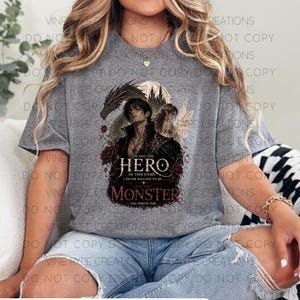 May include: A gray t-shirt featuring a graphic design with the text "I'm not the hero of this story, I never wanted to be... I'm the monster you wrote for." The design includes a dark-haired figure, a fairy, and roses.