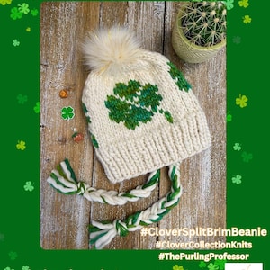 Op de afbeelding: Een witte gebreide beanie met een groen klavertjevier-ontwerp en een witte pompon. De beanie heeft een gespleten rand en is gemaakt met een groen en wit garen.