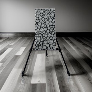 May include: A black metal easel with a white and black patterned board. The board is covered in a repeating pattern of circles.