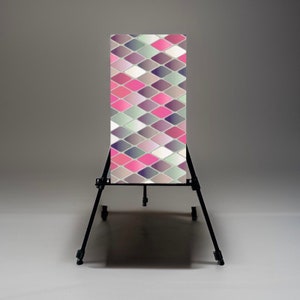 Puede incluir: Un soporte de metal negro con ruedas que sostiene un telón de fondo vertical con un patrón geométrico de diamantes rosas, morados y grises.