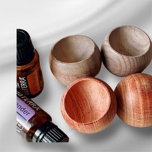May include: Four small, round wooden bowls in varying shades of brown, alongside two essential oil bottles. One bottle is labeled "Wild Orange" and the other "Lavender". The bowls have a smooth, polished finish.