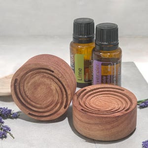 May include: Two wooden diffuser discs with a spiral design, next to two glass bottles of essential oil. The bottles are labeled "Lime" and "Lavender" and are 15 ml each.