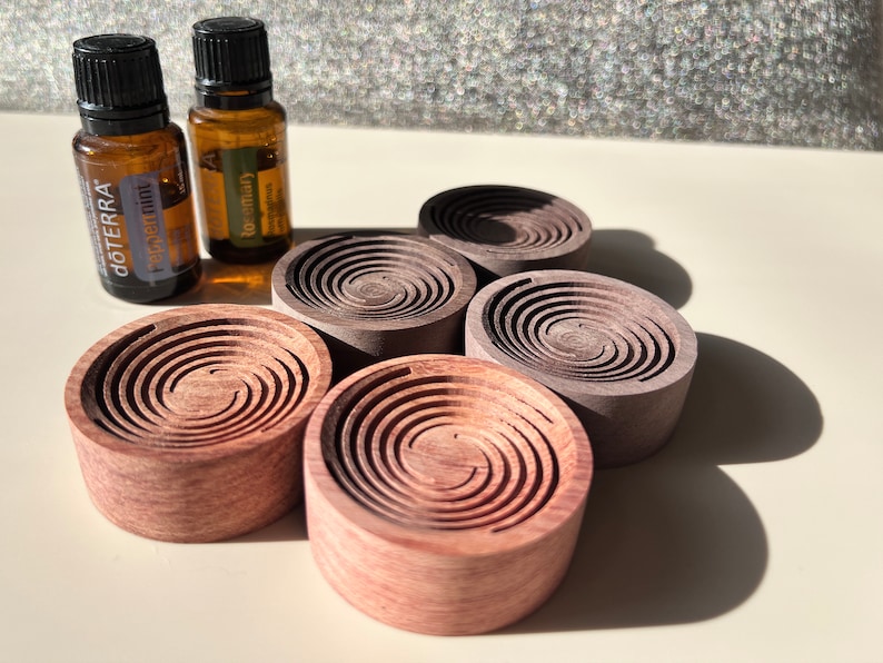 May include: An assortment of wooden essential oil diffusers in various shades of brown and pink. Two small amber glass bottles with black caps are visible, one labeled "dōTERRA Peppermint" and the other "Rosemary". The diffusers have a spiral design.