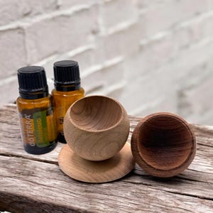 May include: Two brown glass bottles with black caps labeled "doTERRA" and "Melaleuca" sitting on a wooden surface next to two wooden essential oil diffusers.
