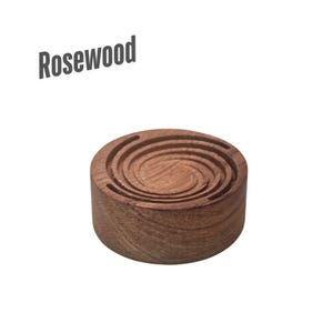 May include: A round, rosewood-colored wooden coaster with a spiral design carved into the top. The word "Rosewood" is printed in gray at the top left. The coaster is a solid, decorative item.