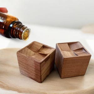 May include: Two wooden blocks with a geometric design, sitting on a wooden surface. A bottle of essential oil is being poured onto the blocks.