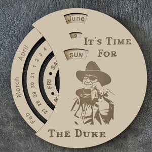 Peut inclure: Un calendrier en bois avec un cadran rotatif présentant les mois de mars, avril, juin et février. Le calendrier a un design d'un homme portant un chapeau de cowboy et des lunettes de soleil avec le texte "It's Time For The Duke".