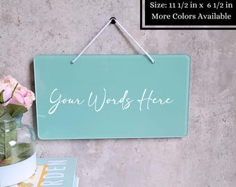May include: A rectangular, light teal sign with the text "Your Words Here" in white script. The sign is 11.5 x 6.5 inches and hangs from a white cord. The text "More Colors Available" is in a black box.
